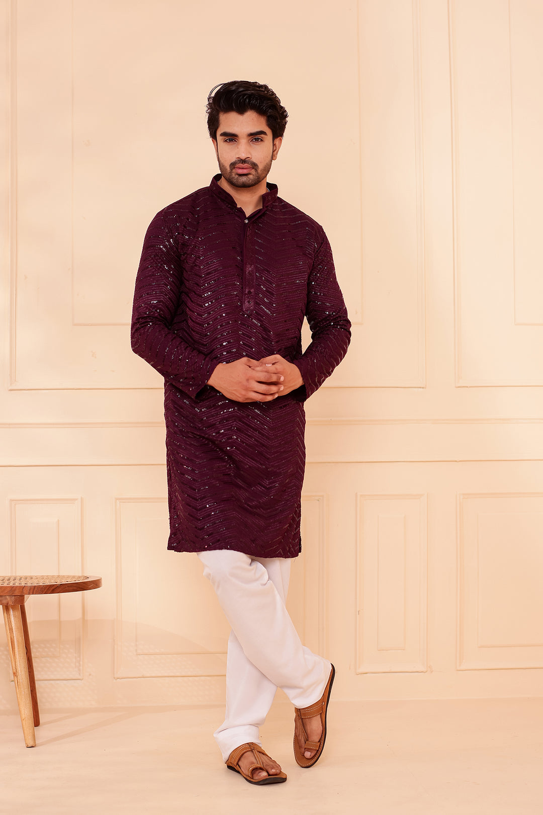 Man wearing a Plum  traditional outfit against a beige wall.