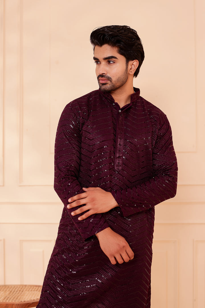 Man wearing a Plum traditional outfit against a beige wall.